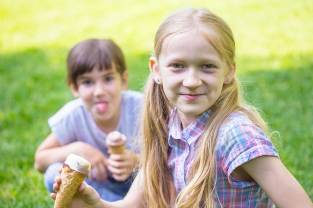 Novias de niñas sonrientes sentados en el césped y comiendo helado. vacaciones de los niños