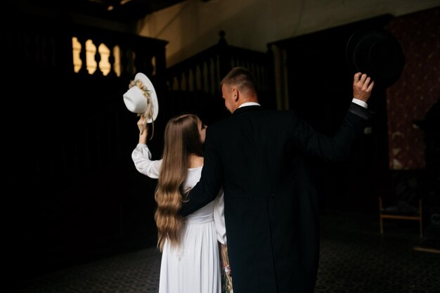 Las novias sostienen sombreros en sus manos Niña en un vestido de novia blanco y sombrero con un ramo de flores La novia y el novio van y sostienen un paraguas Novias en el fondo del castillo