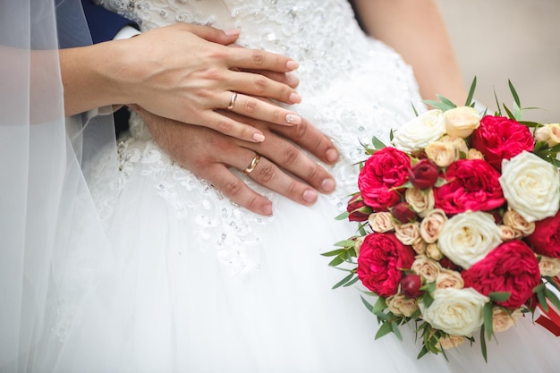 El novio abraza a la novia con anillos de ramo de rosas blancas rojas en manos de una pareja de recién casados