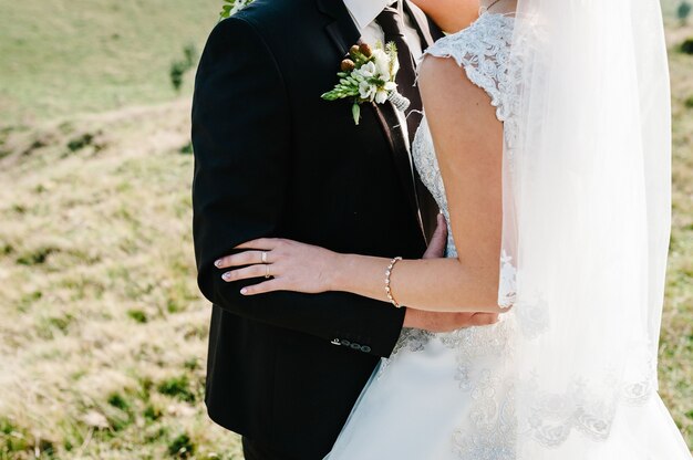 El novio abraza a la novia con las manos detrás de la cintura y de pie en la ceremonia de la boda al aire libre en el patio de la naturaleza.