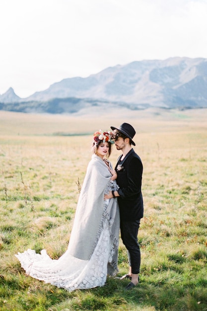 El novio abraza a la novia en un plaid en un campo verde