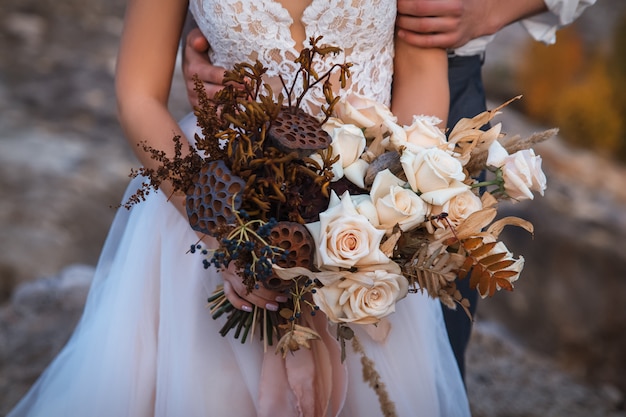 El novio abraza a la novia, que tiene en sus manos un ramo de flores secas.