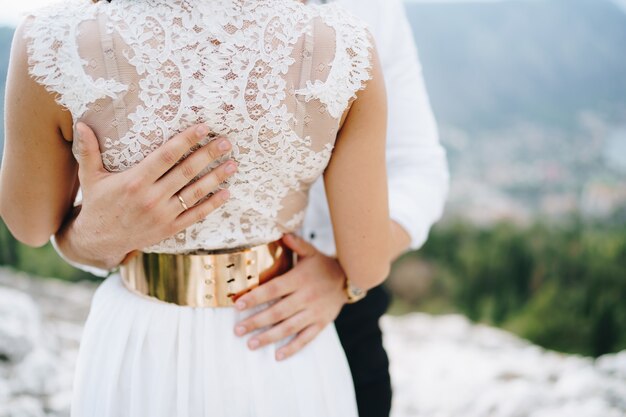 El novio abraza suavemente las manos de la novia del novio en la cintura del primer plano de la novia