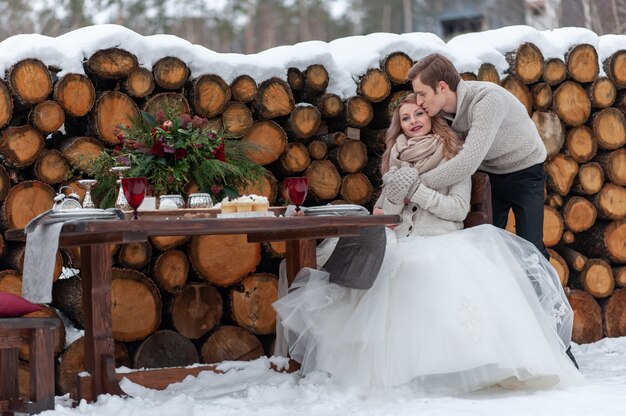 El novio abraza tiernamente a su novia desde atrás en el fondo de la decoración de la boda de invierno