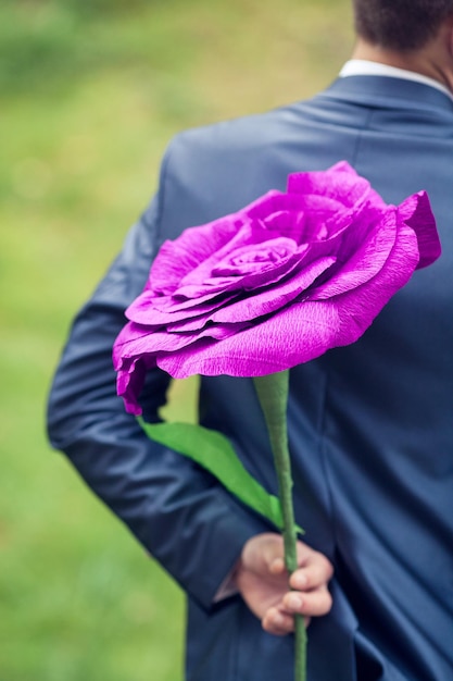 El novio con chaqueta está de pie con una enorme flor hecha de papel crepé en la mano.