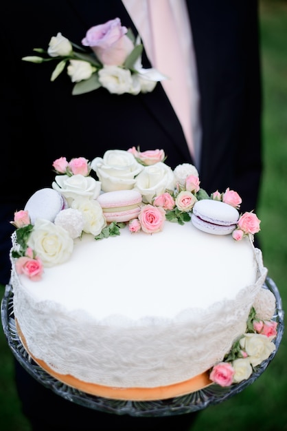 El novio se coloca con el pastel de bodas en el jardín