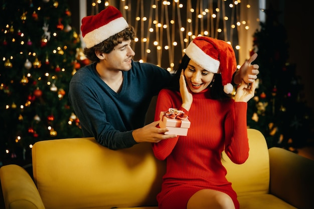 Novio dando un regalo de Navidad a su novia. Pareja joven celebrando en casa. Hombre mujer sorpresa.