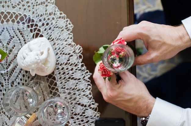 El novio decora las copas de boda con flores.