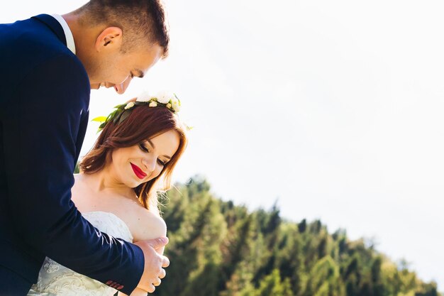 El novio elegante abraza a una novia hermosa con un vestido largo en la espalda