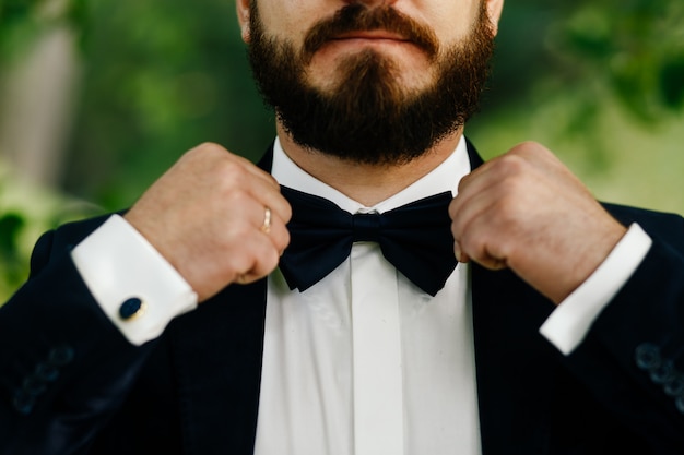 El novio escupe una pajarita negra. hombre con las dos manos toca una corbata de moño