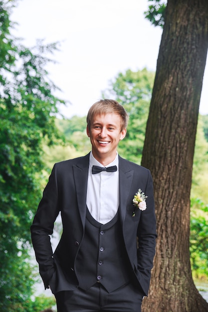 Novio en esmoquin de boda sonriendo y esperando la novia. novio rico en el día la boda. elegante novio en traje y corbata de moño. | Foto Premium