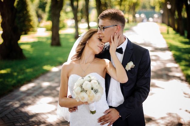 Novio con gafas y novia con un ramo de peonías abrazarse suavemente en el parque