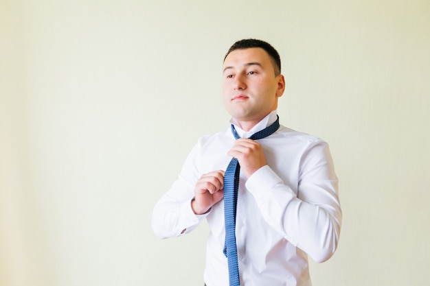 El novio guapo con camisa blanca se pone corbata. el novio