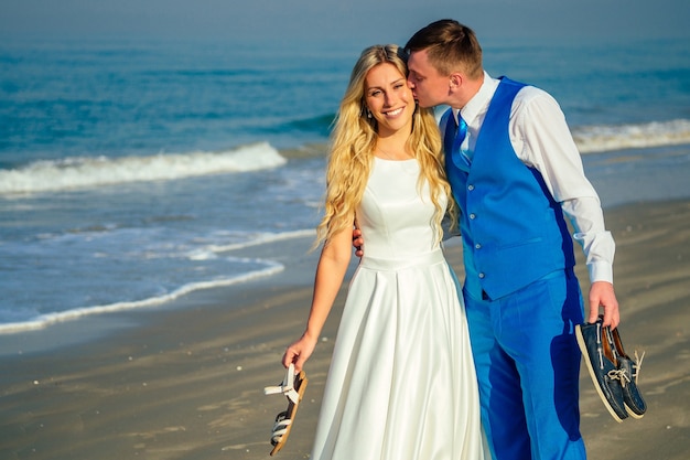 Foto novio guapo con un traje elegante besa a una hermosa novia con un vestido de novia en la playa. concepto de una ceremonia de boda elegante y rica en la playa