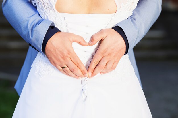 Foto novio haciendo un signo de corazón mientras sus brazos están alrededor de su novia