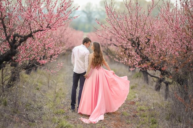 Un novio en un jardín floreciente. Mujer con un vestido largo rosa.