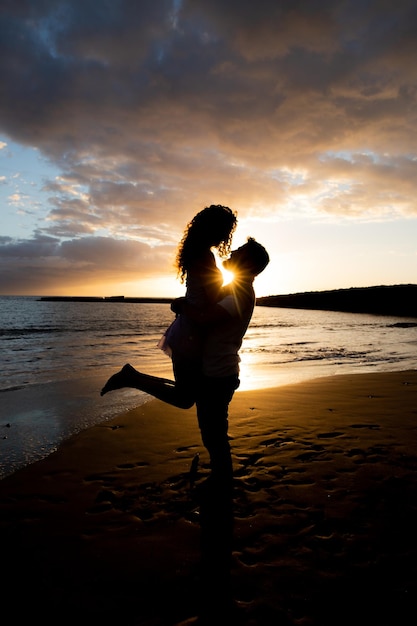 Novio levanta a su novia en la playa durante la puesta de sol y se aman momento romántico entre socios