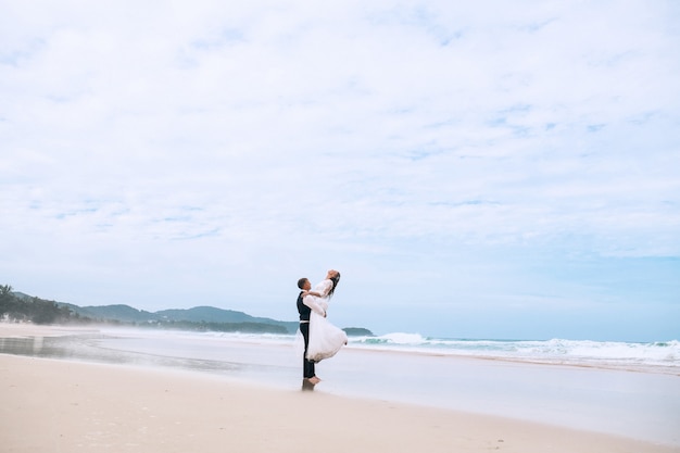 Novio levantando a la novia en sus brazos en una playa tropical