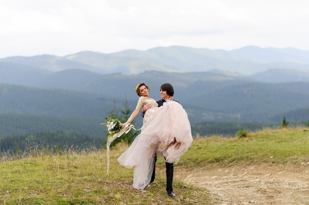 El novio lleva a su novia en sus brazos. Fotografía de bodas en las montañas.