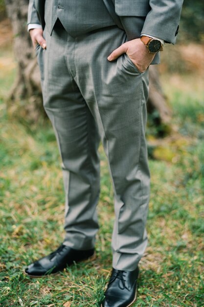 Foto el novio con las manos en los bolsillos de sus pantalones se para en la hierba verde cortada sin rostro