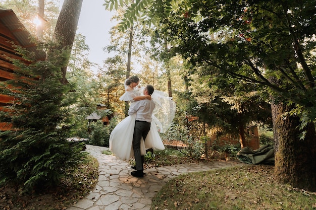 Foto el novio a la moda y la novia linda en vestido blanco con tiara de flores frescas dando vueltas y riendo en el parque jardín bosque al aire libre fotografía de boda retrato de recién casados sonrientes