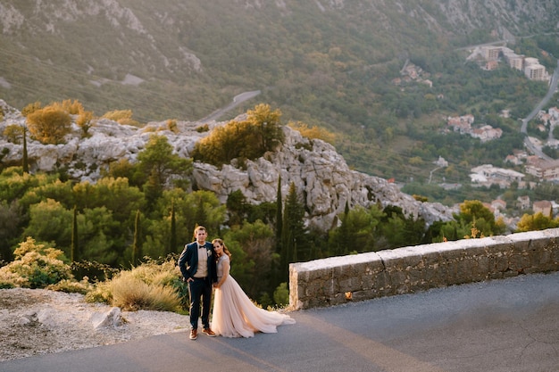 El novio y la novia están abrazados en la carretera en las montañas