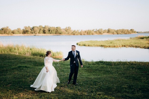 El novio y la novia están caminando en el bosque cerca de un río estrecho en un día brillante