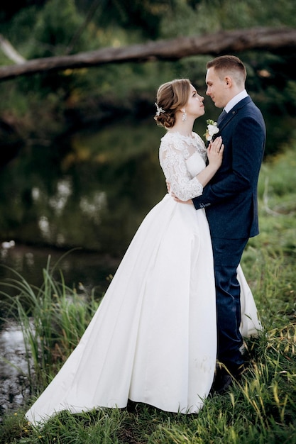 El novio y la novia están caminando en el bosque cerca de un río estrecho en un día brillante