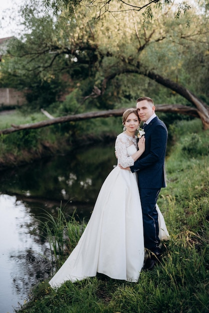 El novio y la novia están caminando en el bosque cerca de un río estrecho en un día brillante