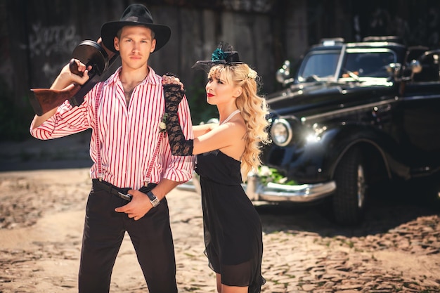 Novio y novia frente a un auto negro pasado de moda