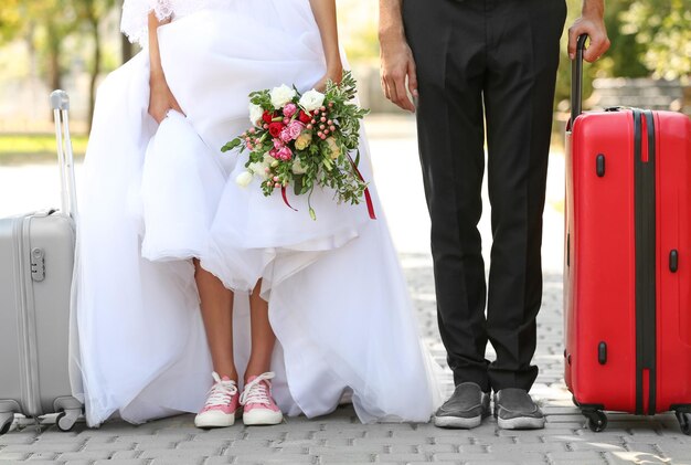 El novio y la novia con maletas caminando por el parque