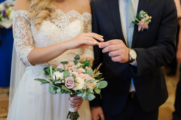 Novio poniendo un anillo de bodas en el dedo de la novia