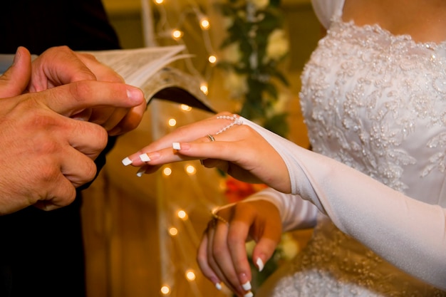 Novio poniendo un anillo de bodas en el dedo de la novia