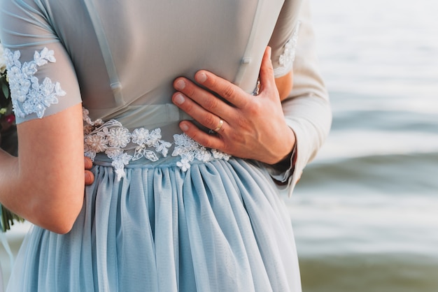 Novio que tiene su mano en la cintura de su novia, parado en una playa