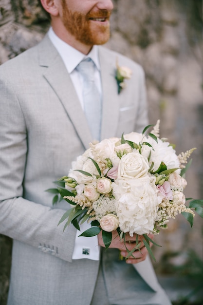 Novio con un ramo de flores está contra un muro de piedra