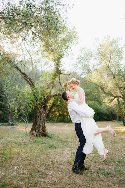 El novio rodea a la novia en sus brazos entre los árboles en el olivar la novia sonríe