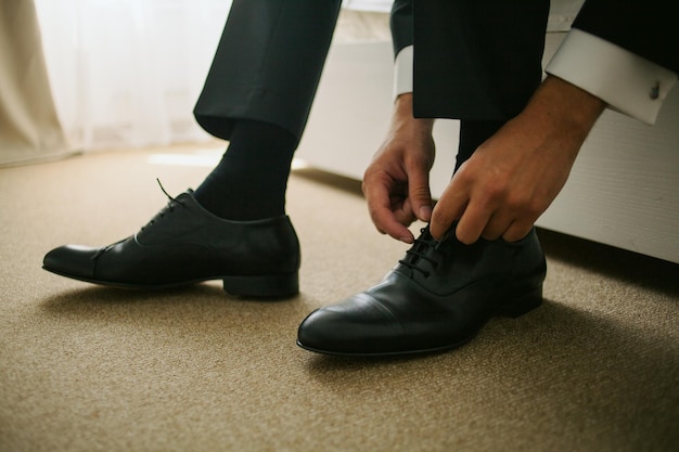 El novio sentado en el sofá y atado los cordones de los zapatos de cuero negro, primer plano. boda