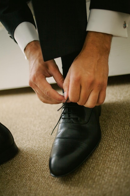 El novio sentado en el sofá y atado los cordones de los zapatos de cuero negro, primer plano. boda