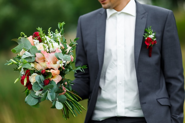 Novio sosteniendo en las manos un ramo de flores de novia de moda