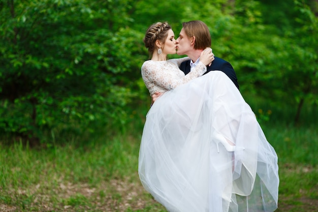 Novio sosteniendo a la novia y besos en el fondo de la vegetación