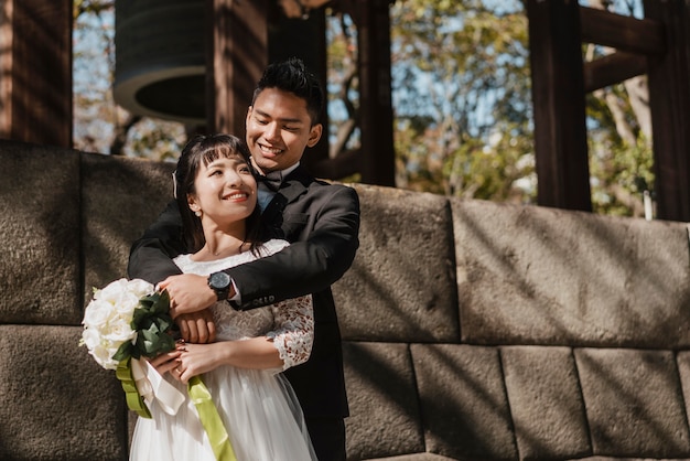 Foto novio sosteniendo a la novia con ramo de flores al aire libre