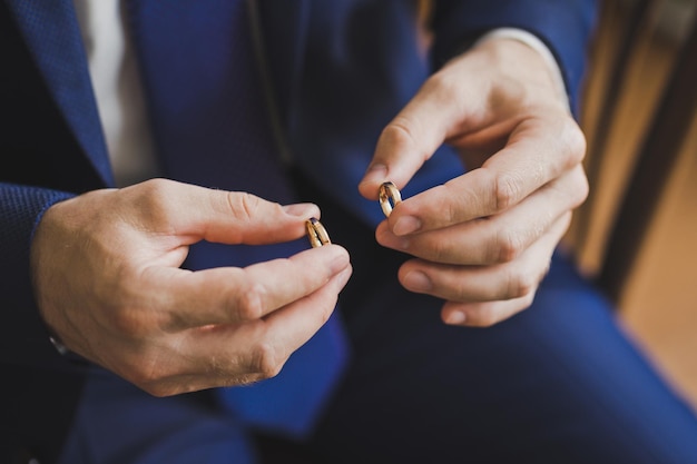 El novio sostiene los anillos de bodas de oro con los dedos 2560