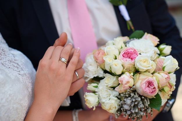 Novio sostiene la mano de su novia y un ramo de novia de cerca