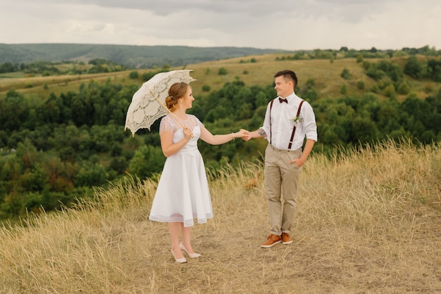 El novio sostiene a la novia de la mano en la boda contra un hermoso paisaje.