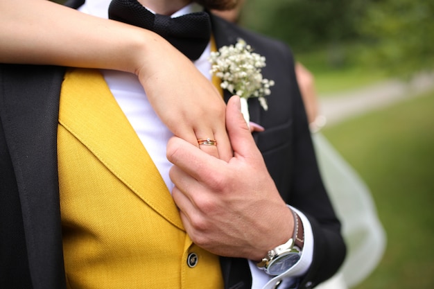 El novio sostiene en su mano la mano de la novia en el dedo de un anillo de bodas de oro.