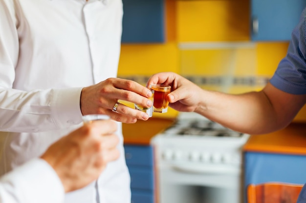 El novio y sus amigos declaran un brindis en la cocina y sostienen vasos de bebidas alcohólicas.