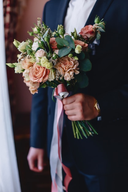 El novio tiene un ramo de boda en sus manos.