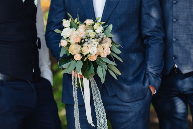 El novio tiene un ramo de boda en sus manos.