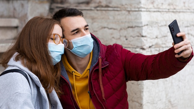 Novio tomando selfie con smartphone en él y su novia mientras usa máscaras