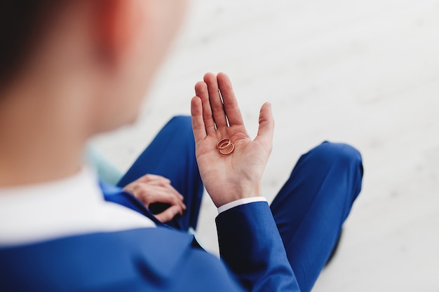 El novio en traje azul tiene anillos de boda en la mano.